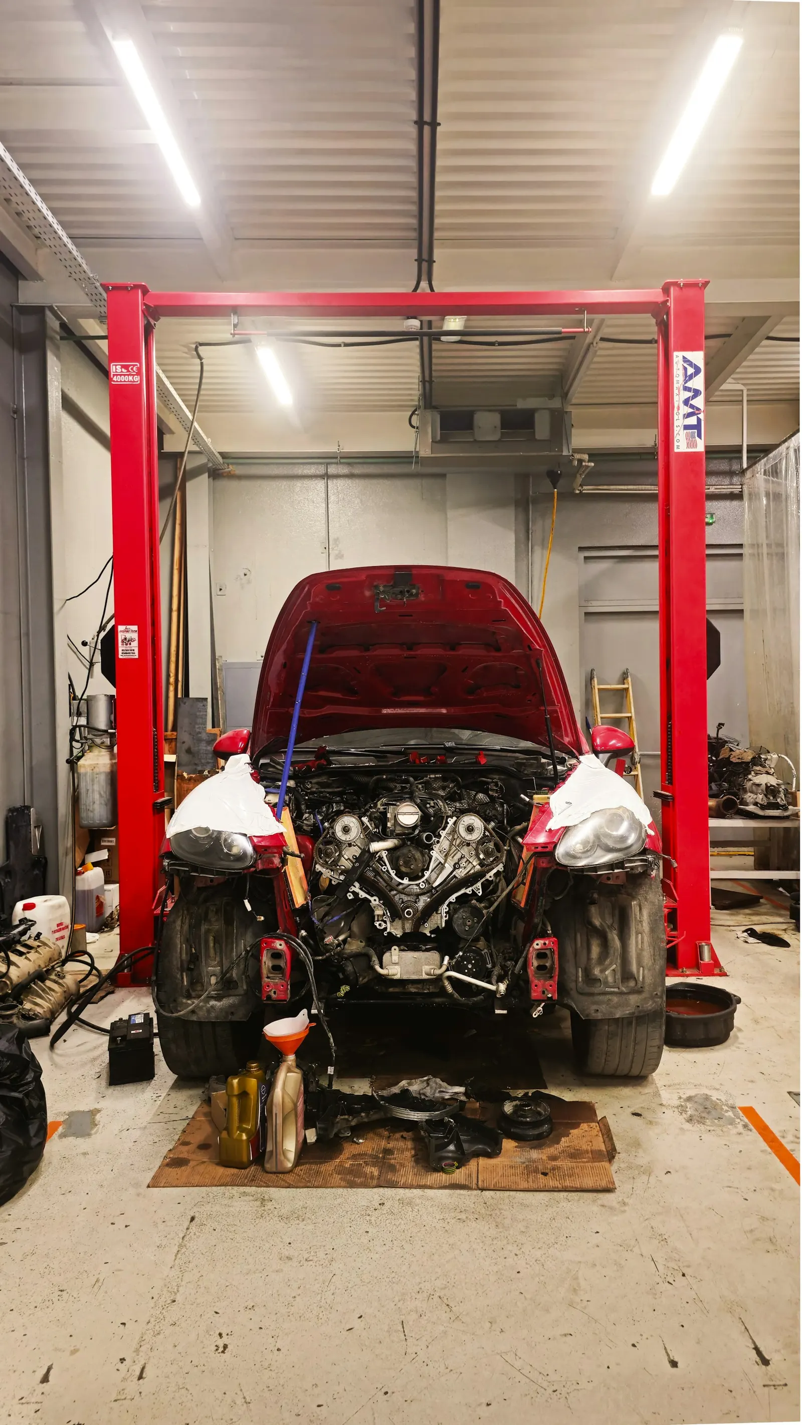 A car on a two-post lift with the engine bay open in a repair shop