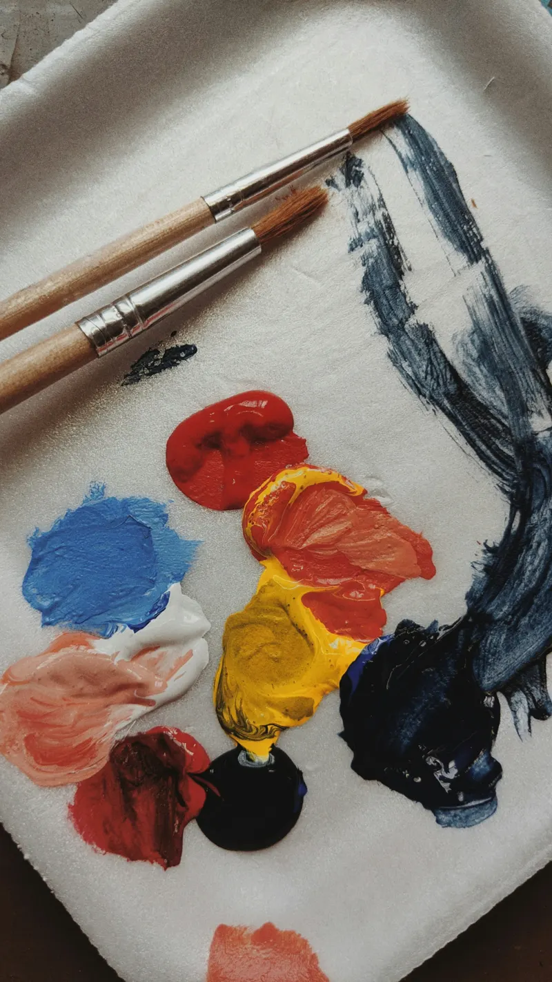 Blobs of red, blue and yellow paint on a palette with brushes