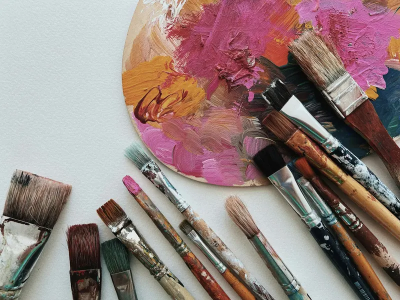 Paint brushes beside a palette of pink and orange paint