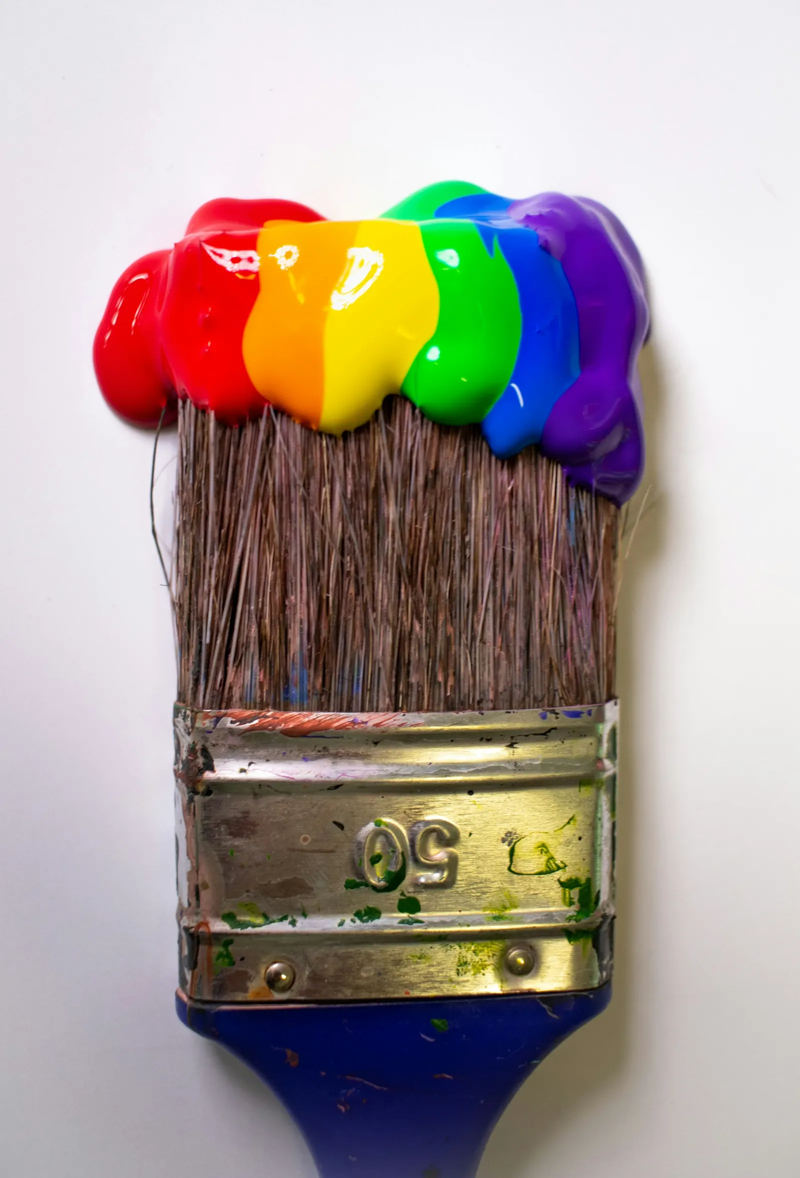 A wide paintbrush loaded with rainbow paint